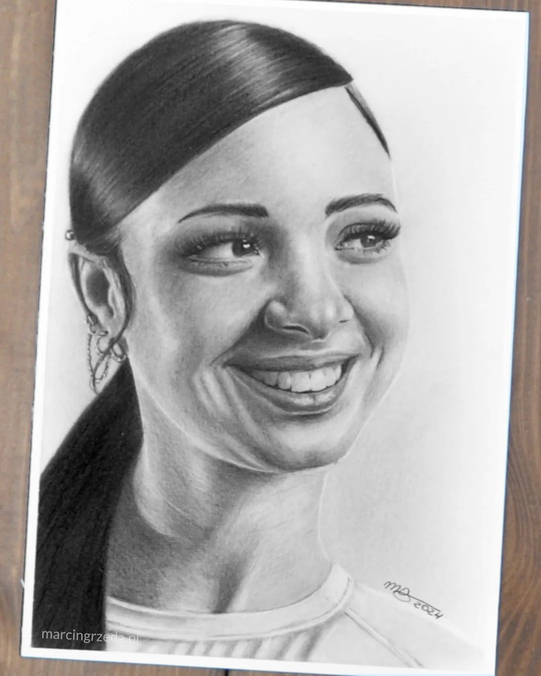 Portret wykonany ołówkiem na formacie A5 przedstawiający uśmiechniętą kobietę z włosami związanymi w kucyk. Jest to przykłąd rysunku na zamówienie.