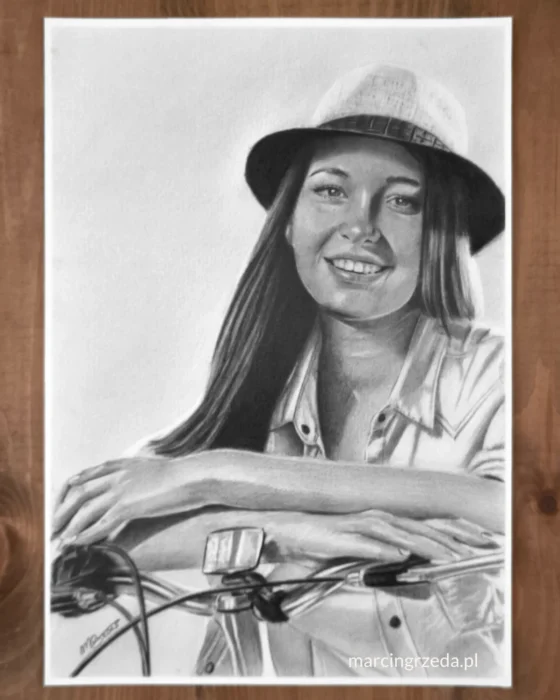 Czarno-biały portret młodej, uśmiechniętej dziewczyny w kapeluszu i na rowerze. Portret wykonany ręcznie ołówkiem na białym papierze formatu A4. Portret ze zdjęcia na zamówienie jako prezent dla dziewczyny.