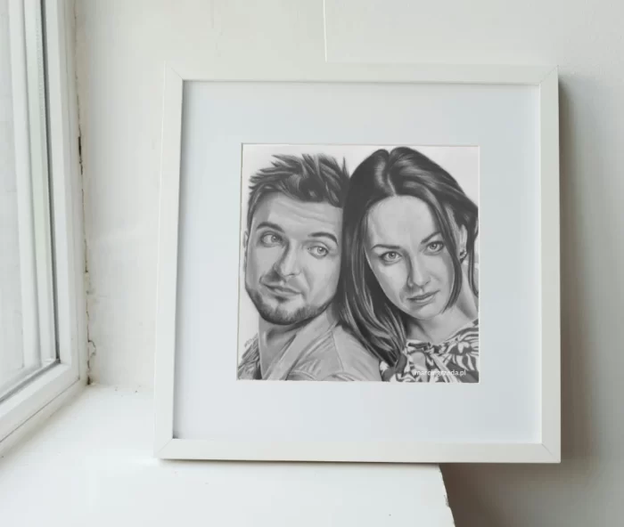 Zdjęcie przedstawia oprawiony portret pary zakochanych wykonany ołówkiem. Biała rama z passe-partout. Portret w ramce postawiony jest na parapecie. Jest to przykład prezentu na Walentynki dla zakochanych.