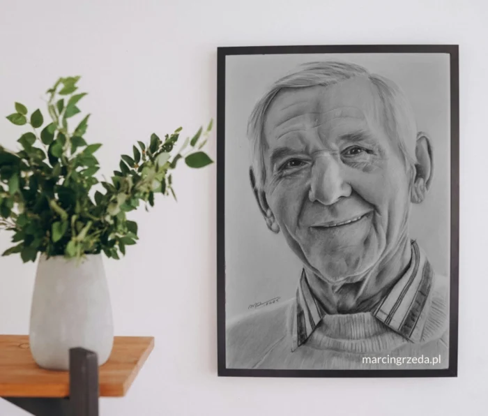 Zdjęcie przedstawiające obraz wiszący na ścianie, na którym narysowany jest portret starszego mężczyzny - dziadka. Portret wykonany jest ołówkiem. Obok obrazu stoi wazon z kwiatami.