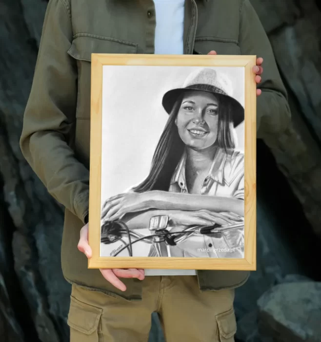 Zdjęcie chłopaka trzymającego oprawiony w drewnianą ramkę portret pięknej dziewczyny w kapeluszu opierającej ręce na kierownicy roweru. 