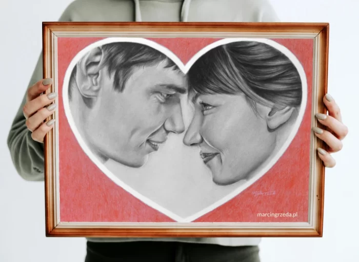 Zdjęcie przedstawia dziewczynę trzymającą portret oprawiony w drewnianą ramkę. Portret wykonany jest ołówkiem na zamówienie i przedstawia parę zakochanych osób patrzących na siebie. Para ta umieszczona jest w sercu otoczonym czerwonym tłem wykonanym kredkami,