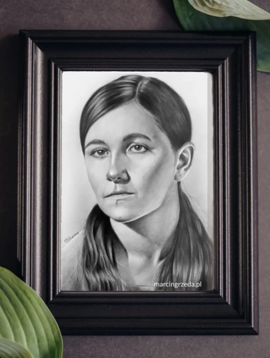 Zdjęcie przedstawia portret młodej pięknej dziewczyny wykonany ołówkiem ze starego zdjęcia na zamówienie. Rysunek jest oprawiony w ramkę. Na zdjęciu widoczny jest także kawałek kwiatka.